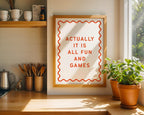 Framed poster with 'Actually it is all fun and games' text in a kitchen setting with plants and shelves.