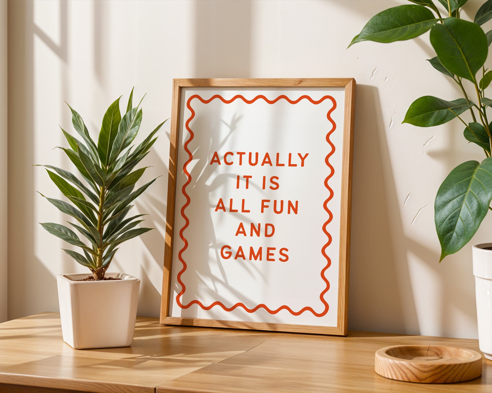 Framed quote 'Actually it is all fun and games' on a wooden surface with plants.