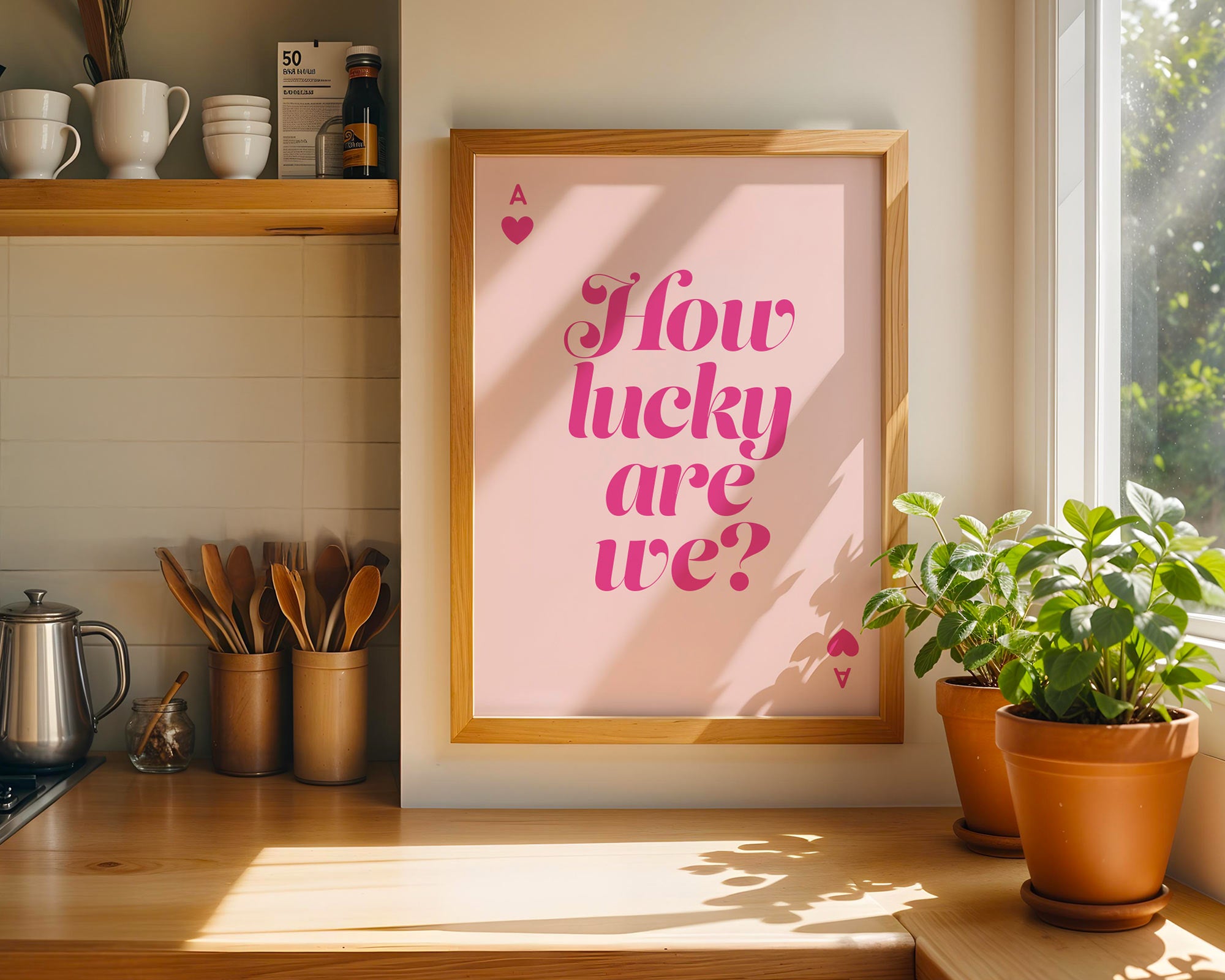 Framed poster with 'How lucky are we?' text in a kitchen setting with plants and cups.