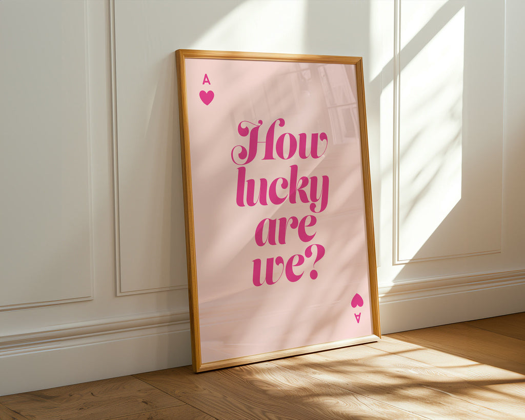 Framed pink poster with 'How lucky are we?' text on a white wall.