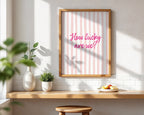 Framed print with 'How lucky are we?' text on a wall with a wooden shelf and plants.