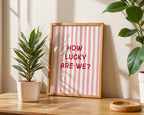 Framed picture with 'How Lucky Are We?' text on a table with plants