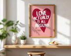 Framed poster with heart design and text on a wall above a wooden shelf.
