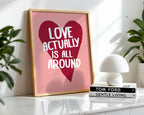 Framed poster with 'Love actually is all around' design on a shelf with books and a lamp.