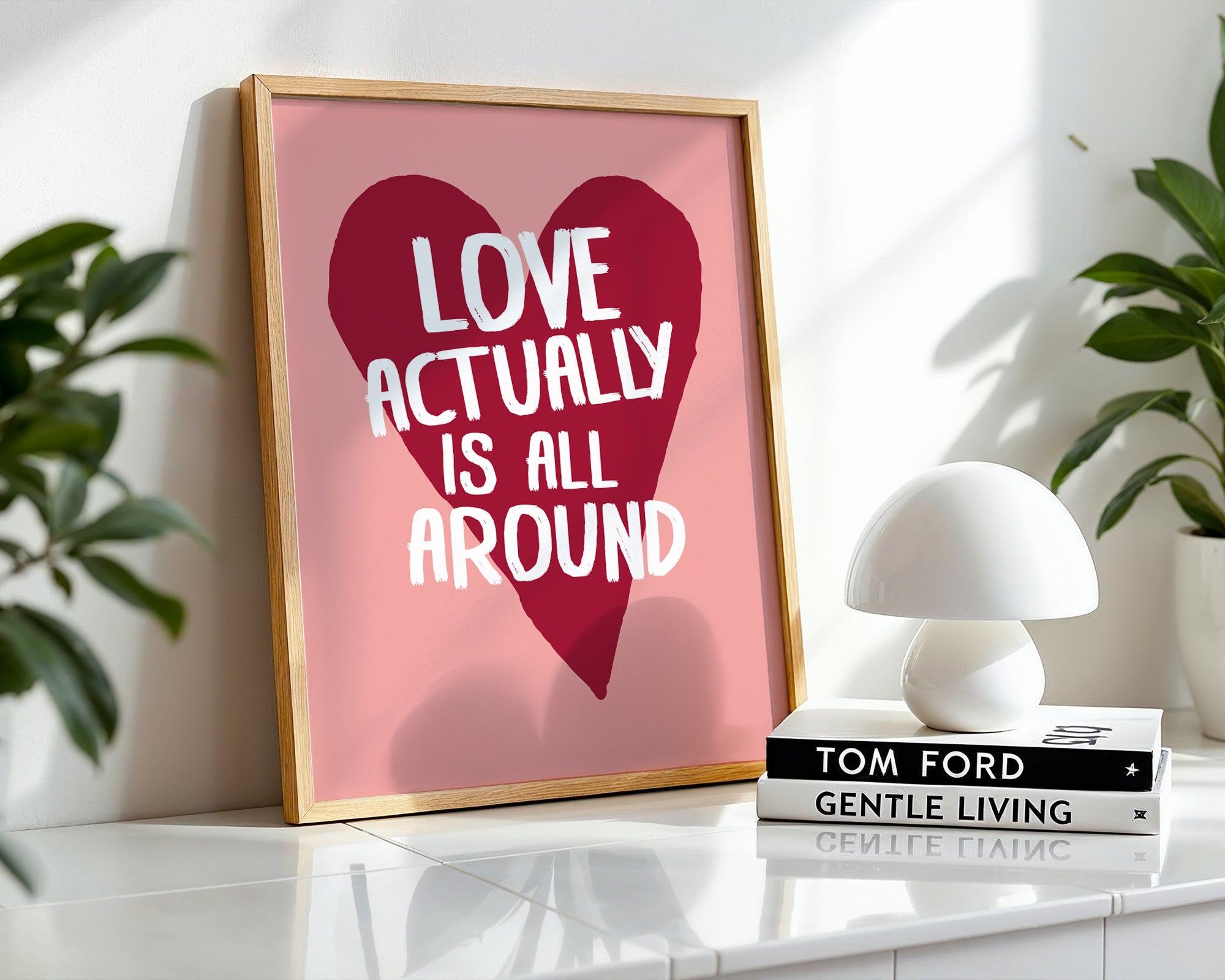 Framed poster with 'Love actually is all around' design on a shelf with books and a lamp.