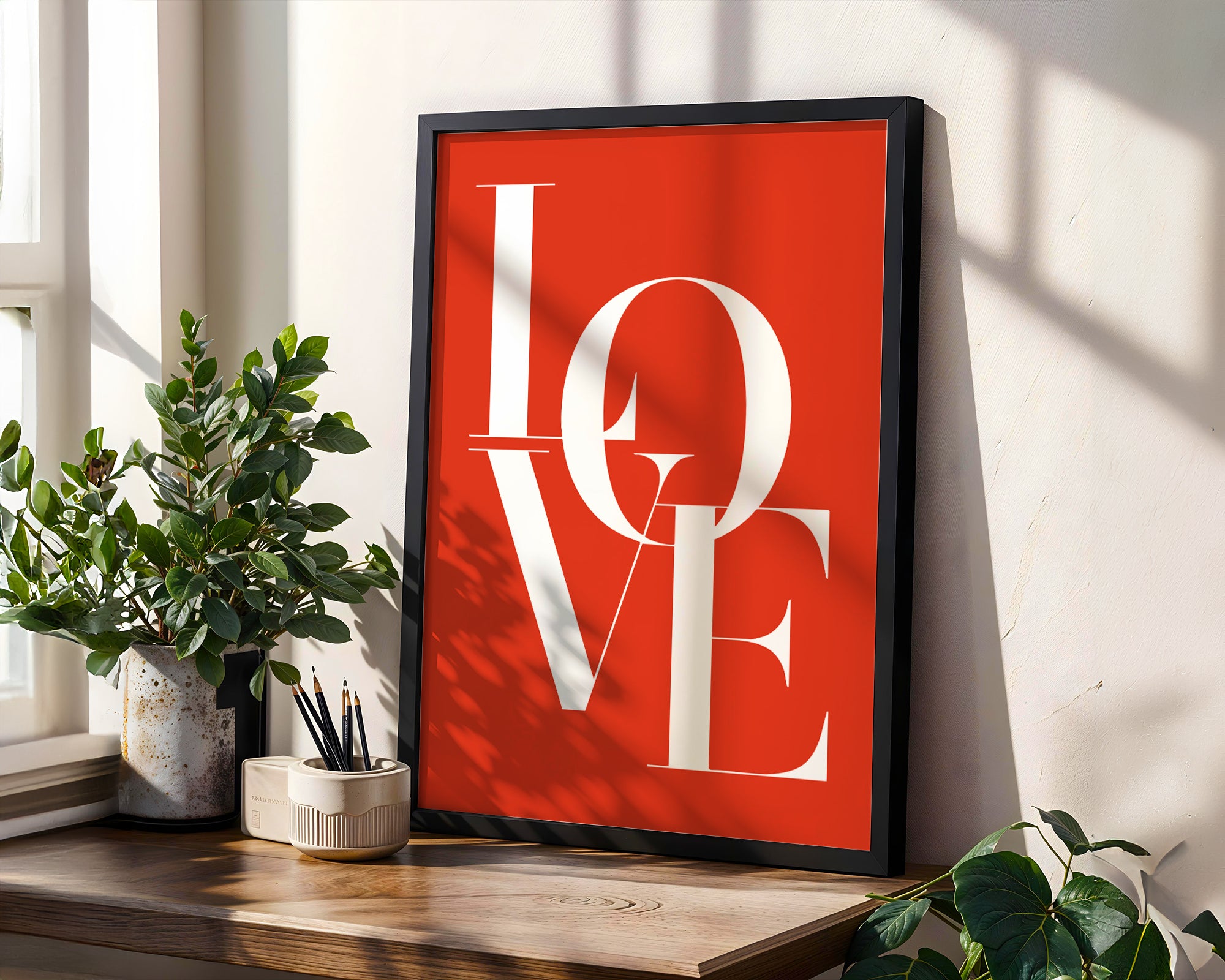 Framed 'LOVE' poster on a wall with plants and a window in the background
