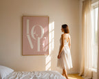 Woman in a white dress standing in a bedroom with a 'LOVE' framed picture on the wall.