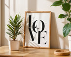 Framed 'LOVE' artwork on a wooden surface with plants