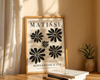Framed Matisse poster with black floral designs on a beige wall.