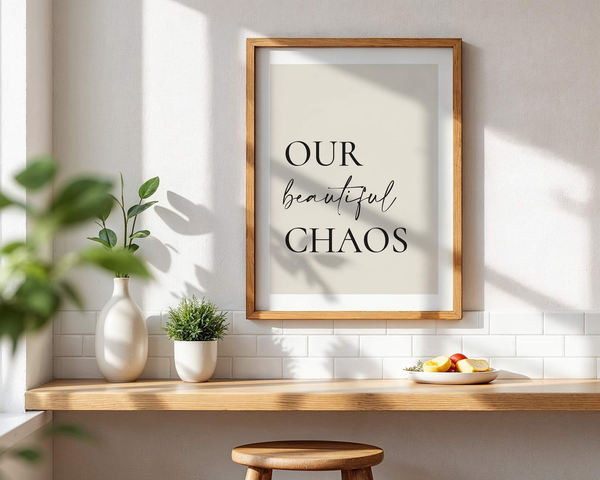 Framed print with 'Our beautiful chaos' text on a wall with a wooden shelf and plants.