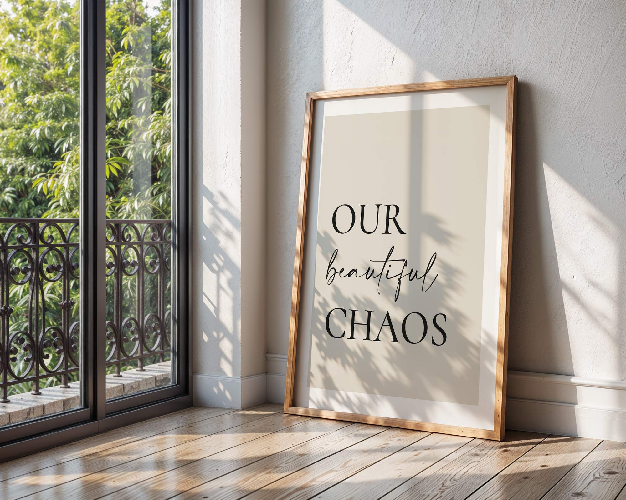 Framed print with 'Our beautiful chaos' text on a wall next to a window with a view of greenery.