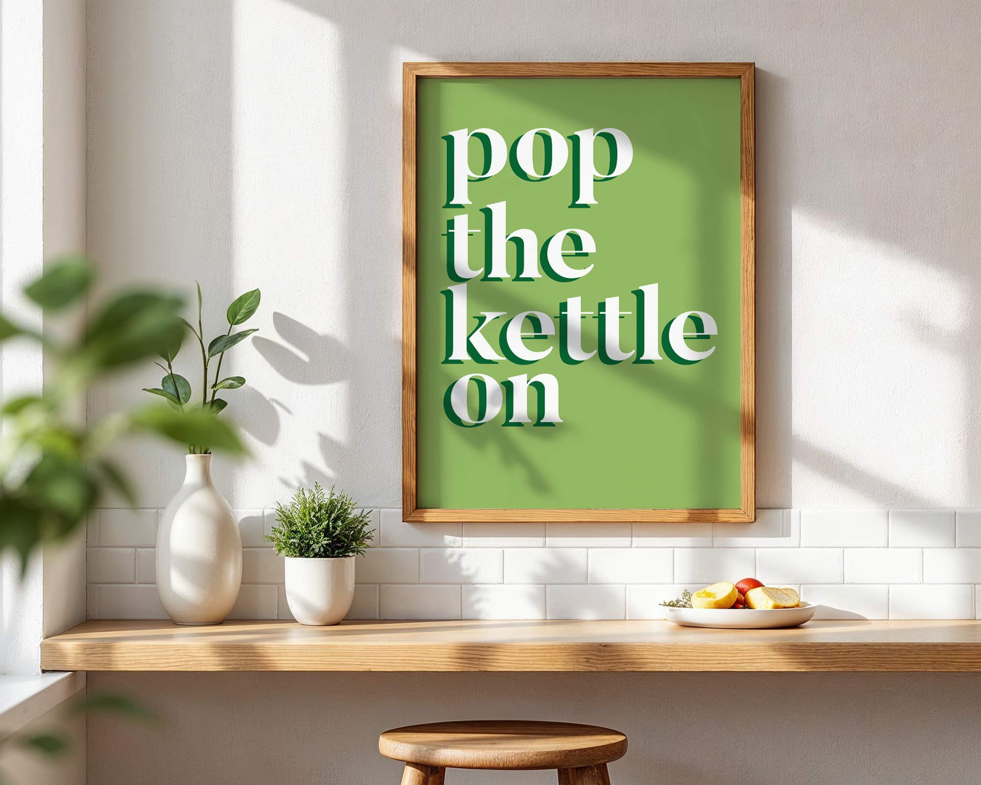 Green framed poster with 'pop the kettle on' text in a kitchen setting