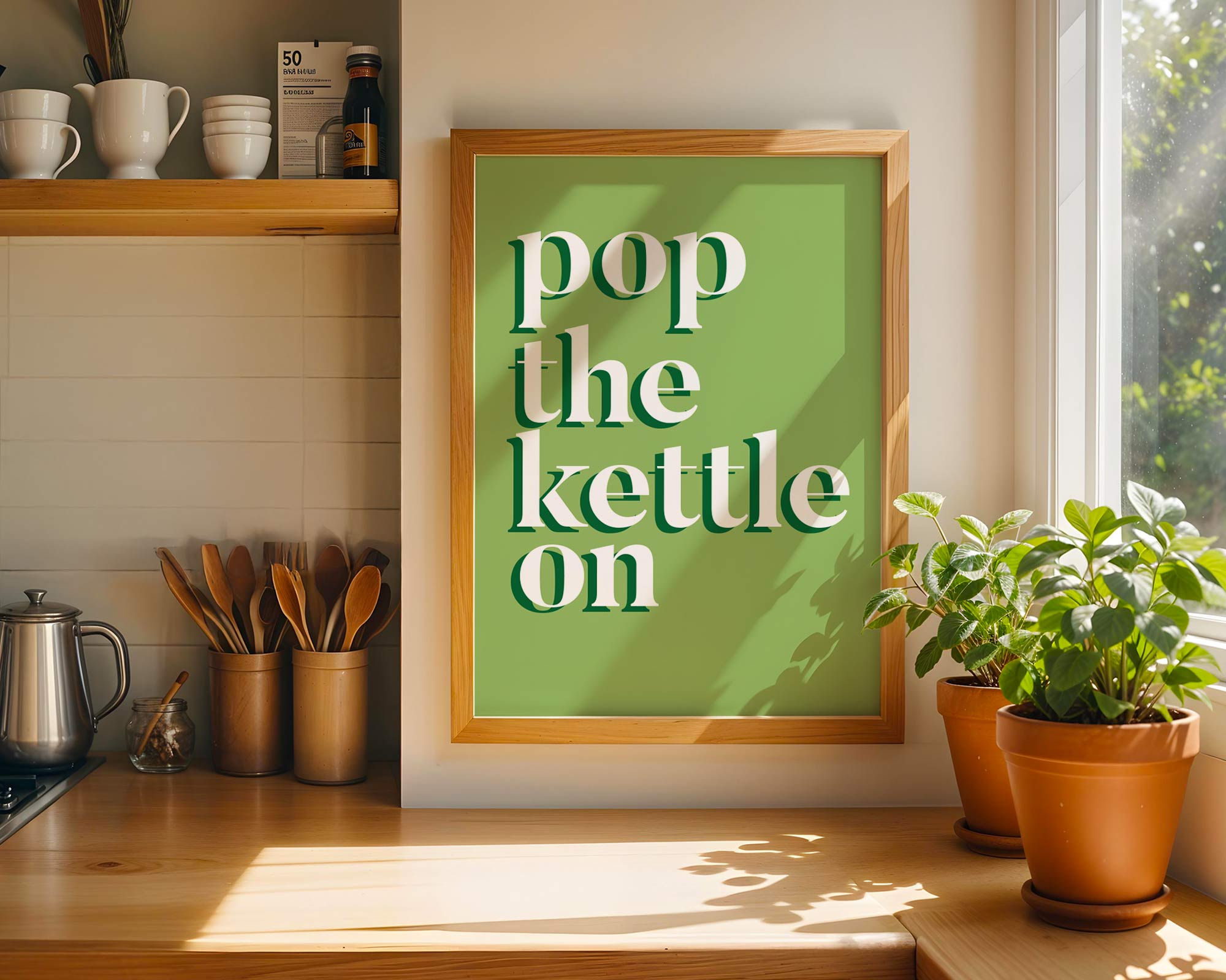 Kitchen counter with a framed print that says 'pop the kettle on', potted plants, and kitchenware.