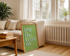 Living room with a 'pop the kettle on' sign, books, and a plant.