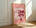 Framed poster with 'Welcome to our beautiful chaos' text on a pink background, leaning against a white wall.