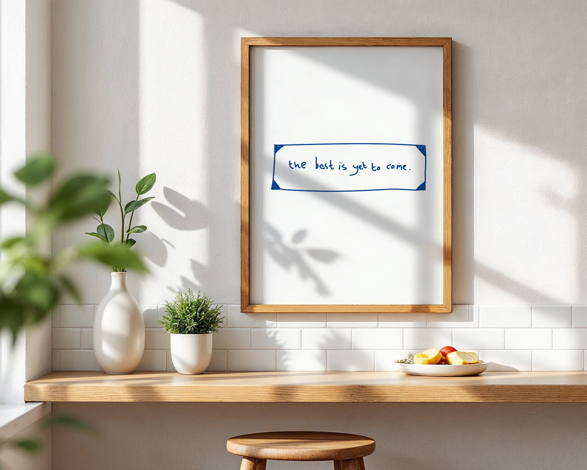 Framed artwork with text on a wall in a room with a wooden shelf and plants.