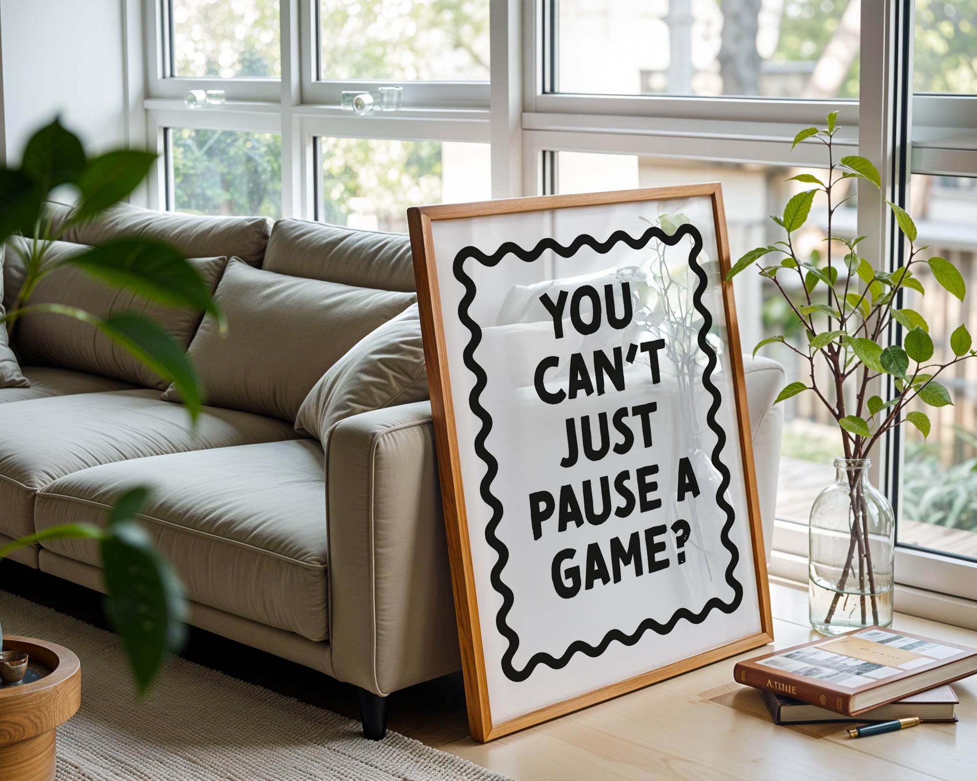 Framed sign with text 'You can't just pause a game?' on a living room table.
