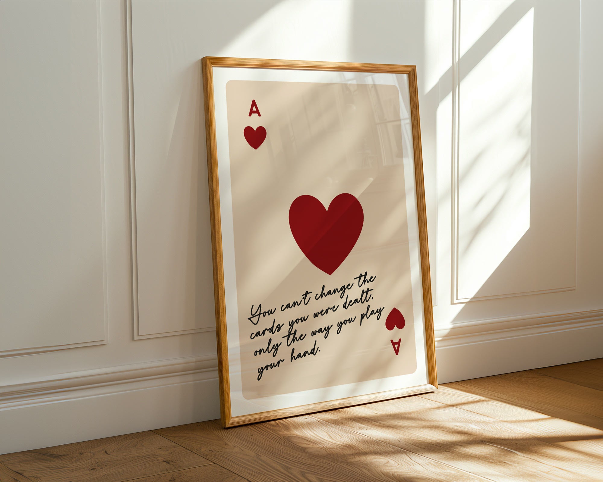 Framed artwork with a red heart and text on a beige background, placed on a wooden floor.