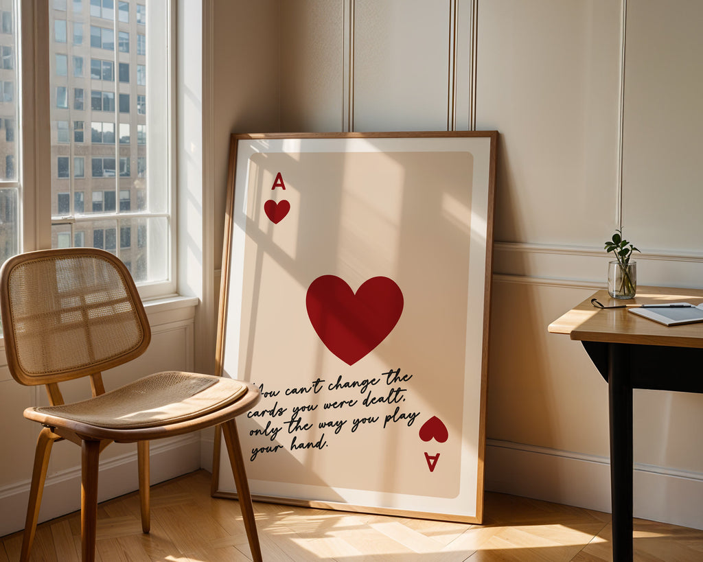 Framed artwork with a red heart and text in a room with a chair and table.