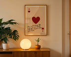 Framed artwork with a red heart and text on a wall above a wooden cabinet with decorative items.