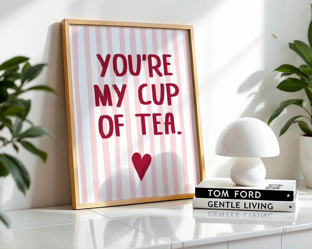 Framed print with 'You're my cup of tea' text on a striped background, placed on a surface with books and a lamp.