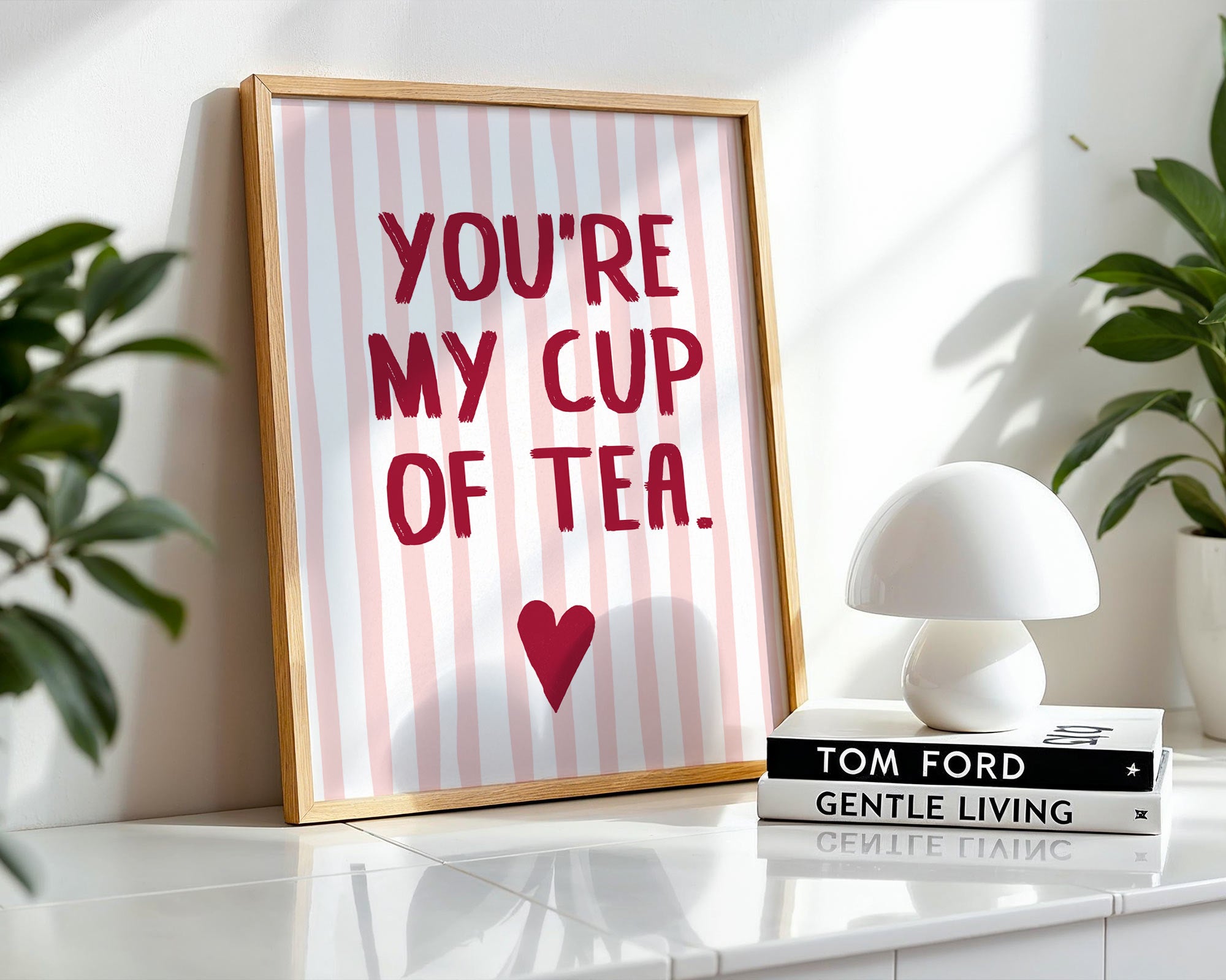 Framed print with 'You're my cup of tea' text on a striped background, placed on a surface with books and a lamp.