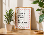 Framed quote 'Don't be a lady, be a legend' on a table with plants