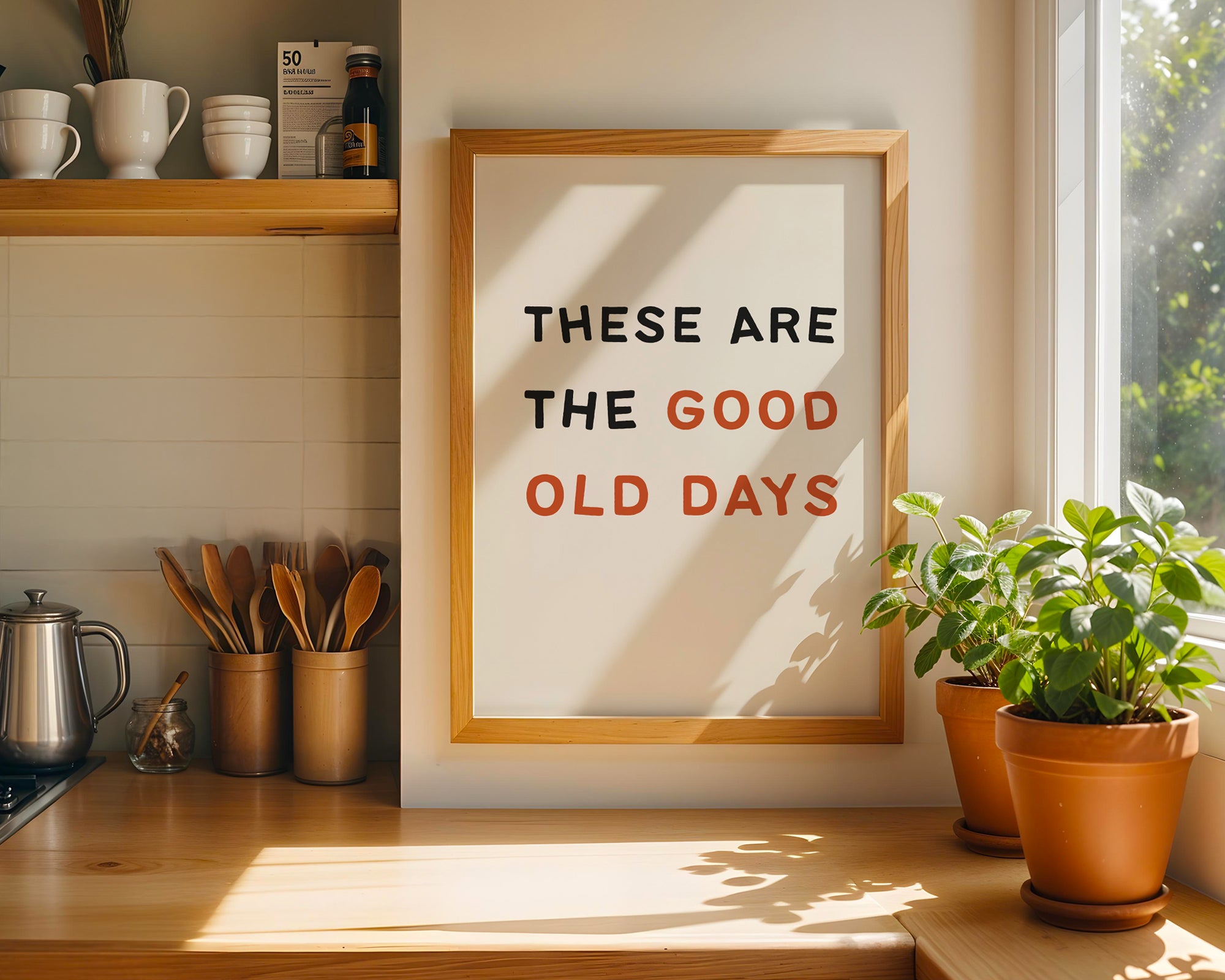 Framed poster with 'These are the good old days' text in a kitchen setting with plants and cups.