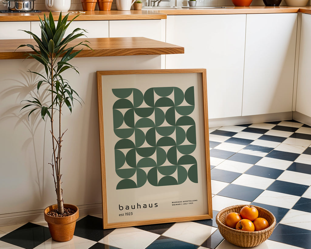 Framed Bauhaus poster on a checkered floor with a plant and bowl of oranges in a kitchen.