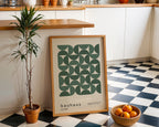 Framed Bauhaus poster on a checkered floor with a plant and bowl of oranges in a kitchen.
