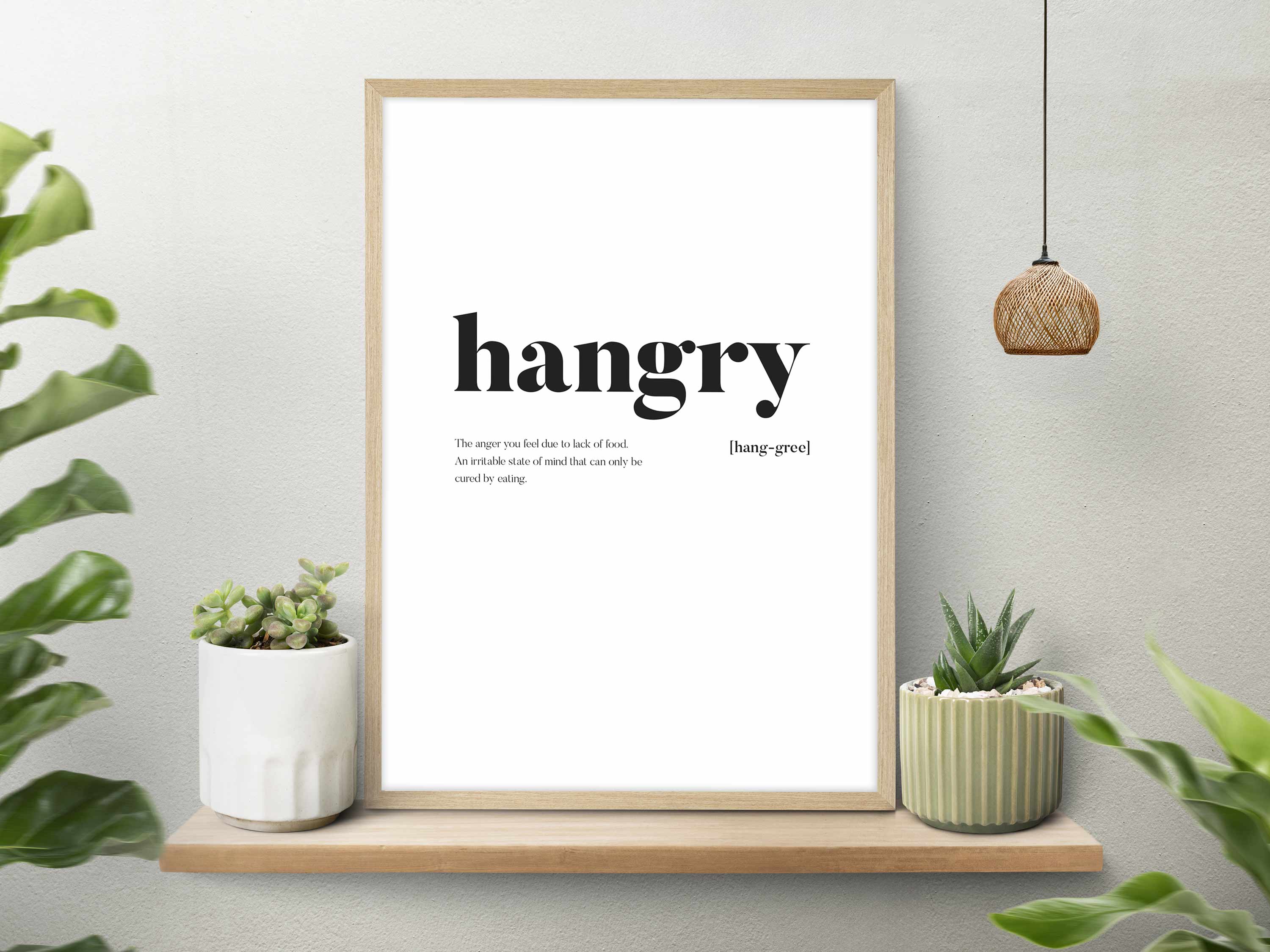 Framed print with the word 'hangry' on a wall with plants around