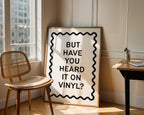 Framed poster with text 'BUT HAVE YOU HEARD IT ON VINYL?' in a room with a chair and table.