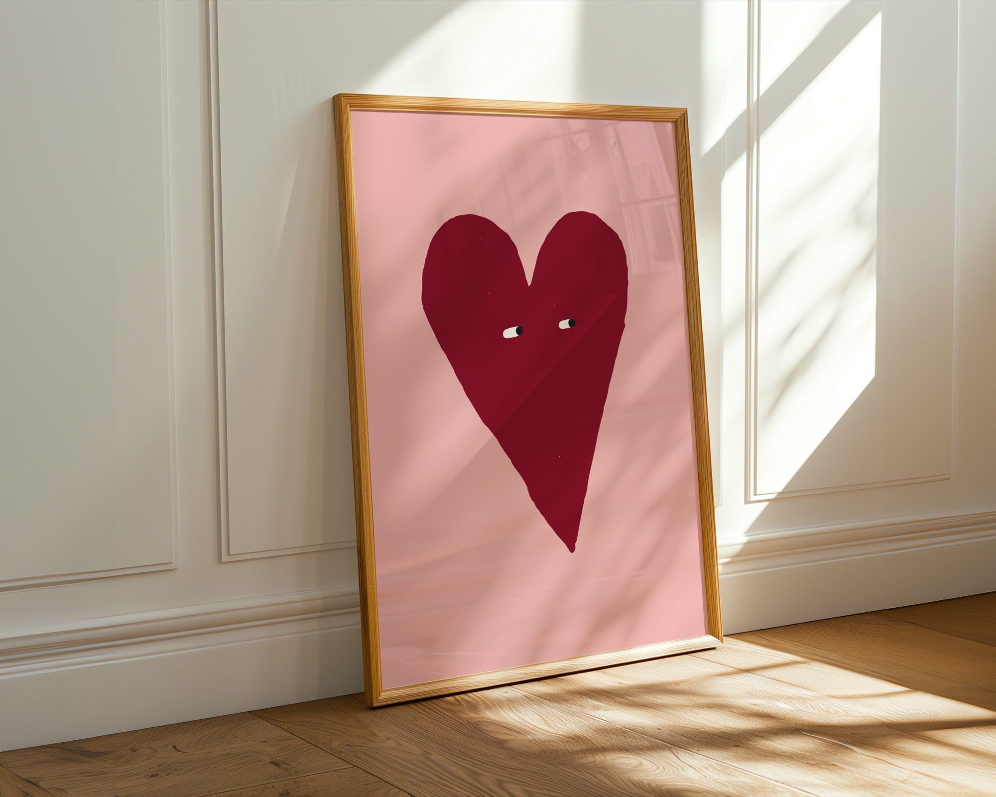 Framed artwork with a red heart on a pink background against a white wall.