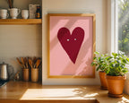 Heart-shaped artwork on a pink background in a wooden frame, placed in a kitchen.