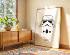 Framed poster of a stormtrooper helmet on a wall in a room with a wooden cabinet and plant.