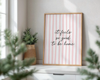 Framed print with 'it feels so good to be home' text on a striped background, placed on a windowsill with plants.
