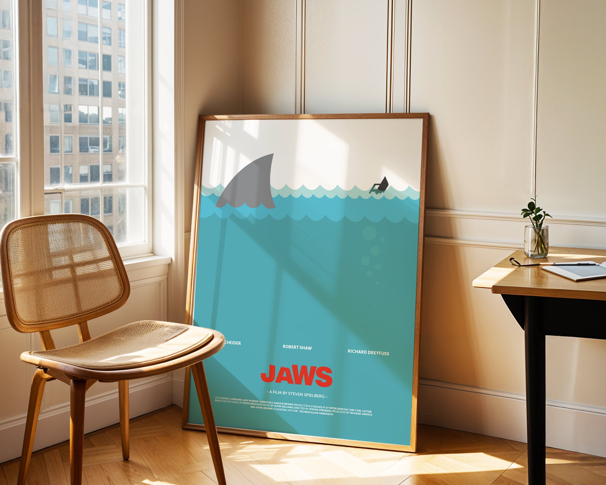 Framed 'Jaws' poster leaning against a wall in a room with a chair and table.
