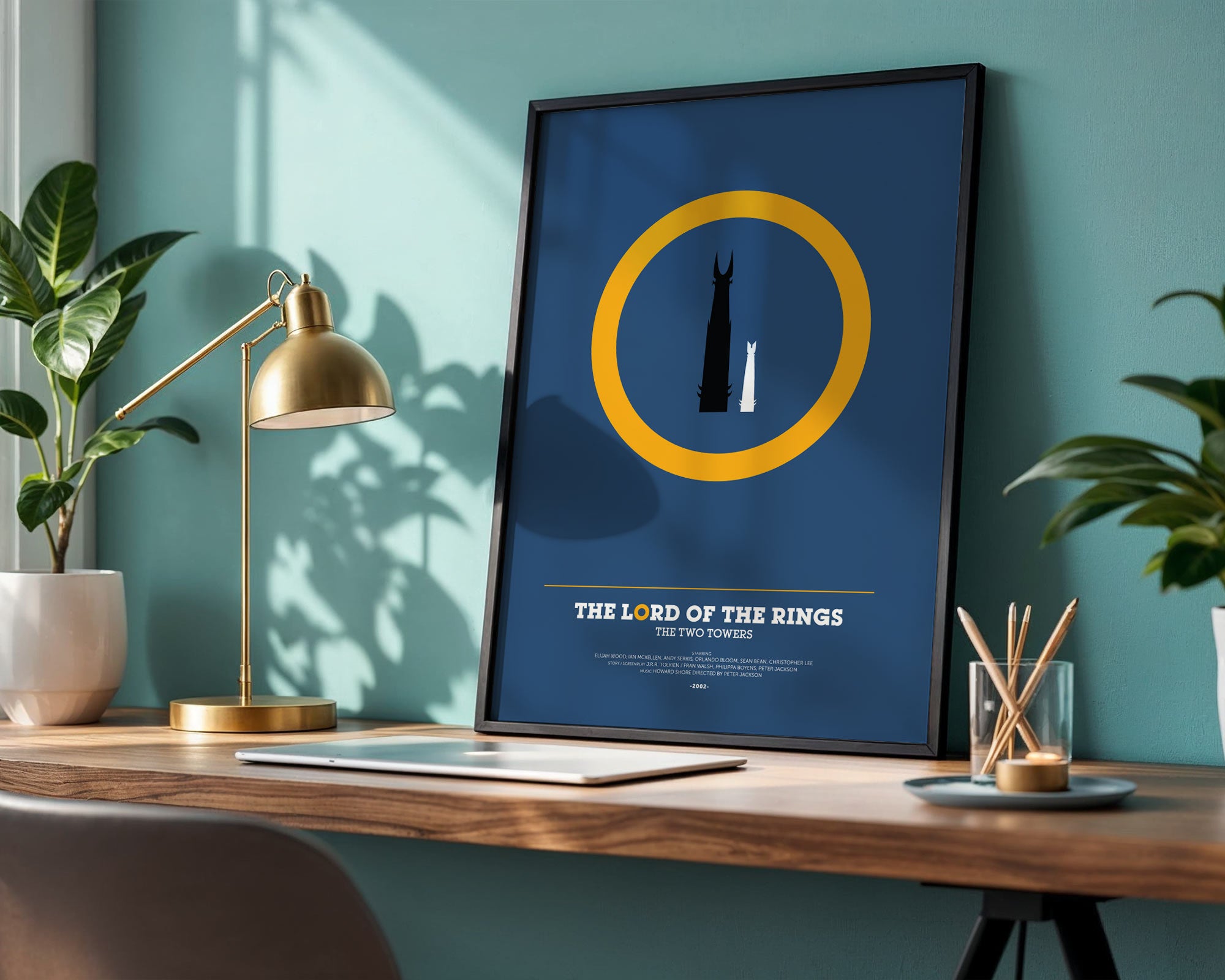 Framed 'The Lord of the Rings' poster on a desk with a lamp and plants.