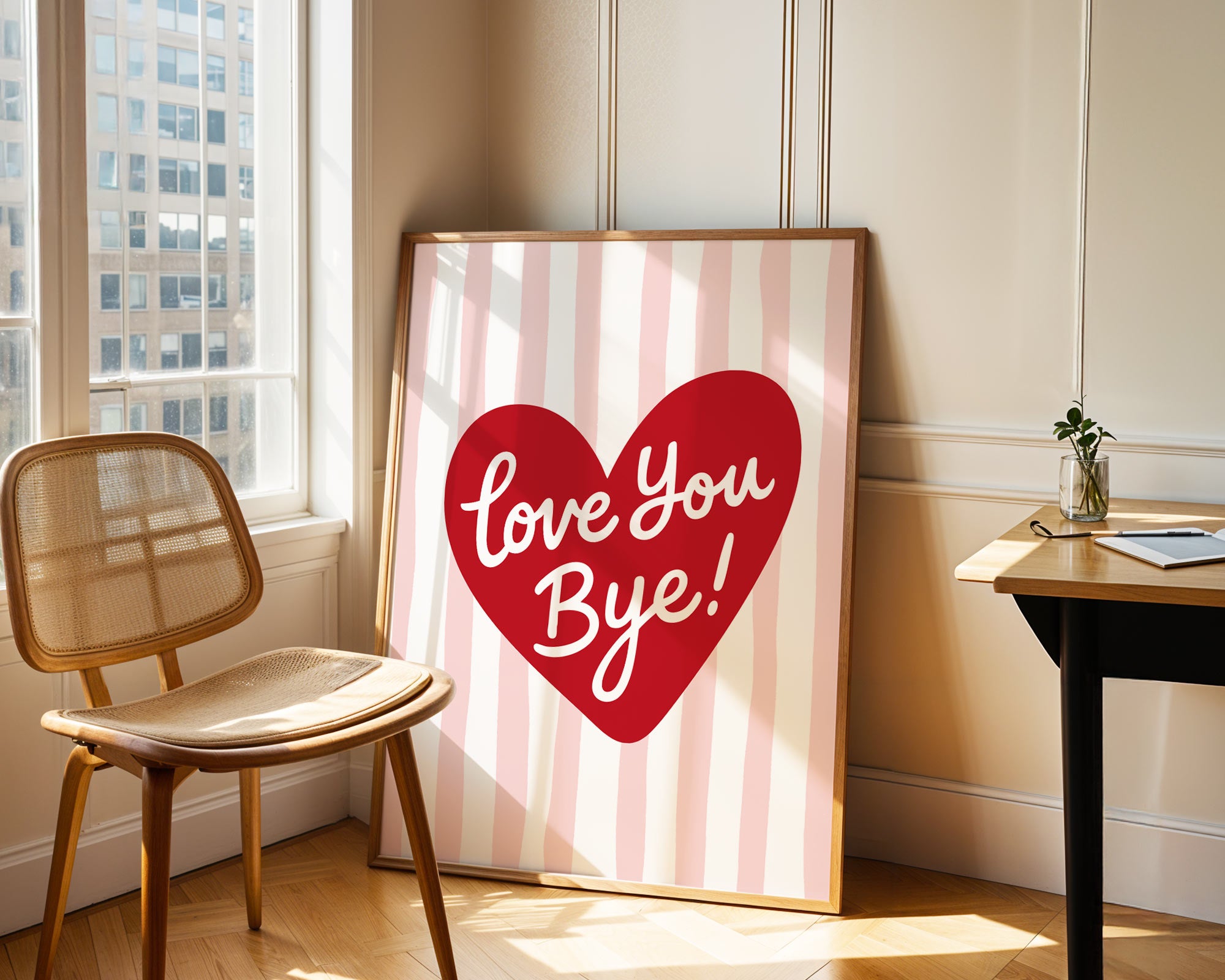 Framed artwork with a red heart and 'Love You Bye!' text in a room with a chair and window.