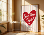 Framed artwork with a red heart and 'Love You Bye!' text in a room with a window and small table.