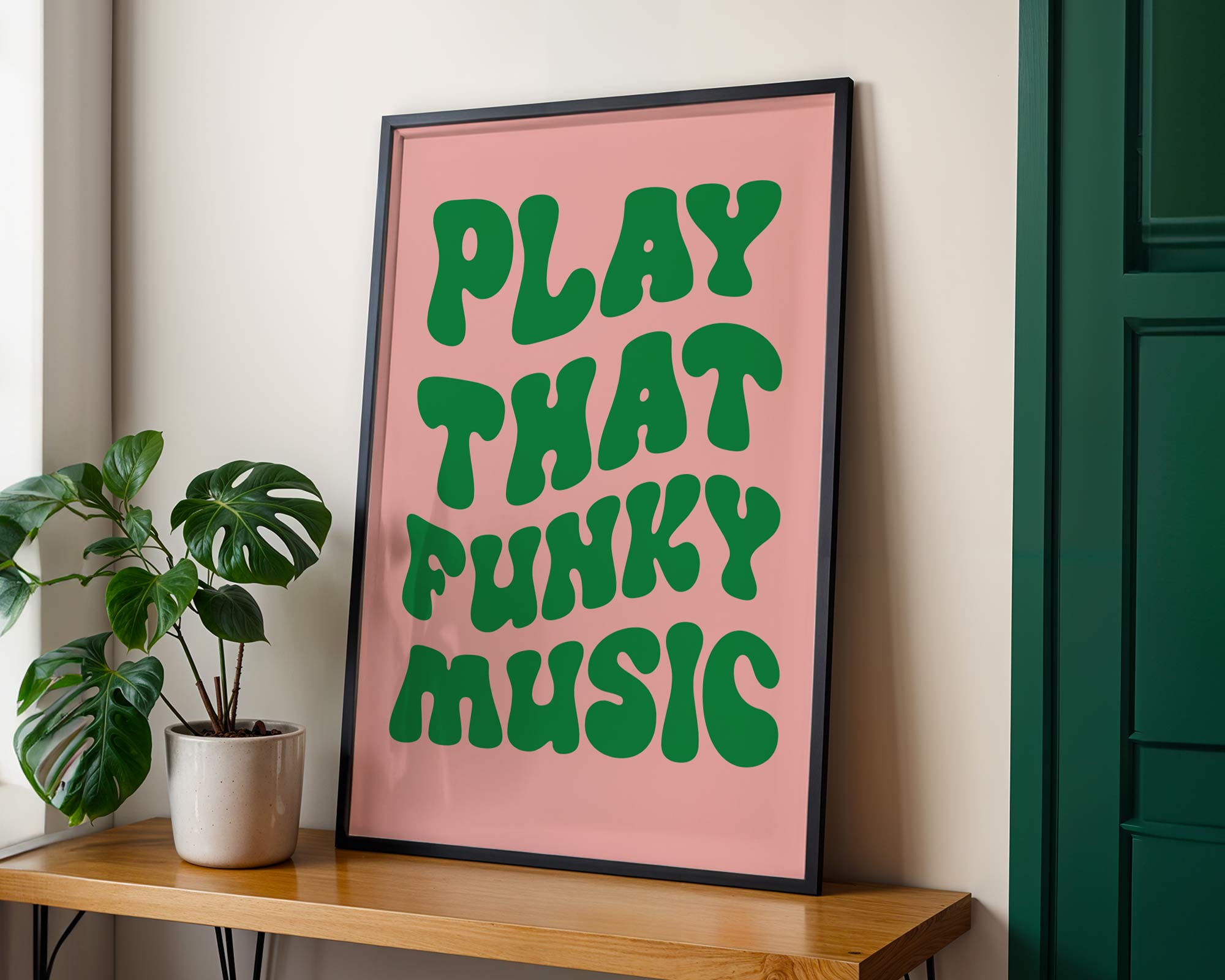 Framed poster with 'Play That Funky Music' text on a pink background, placed on a wooden shelf with a plant beside it.
