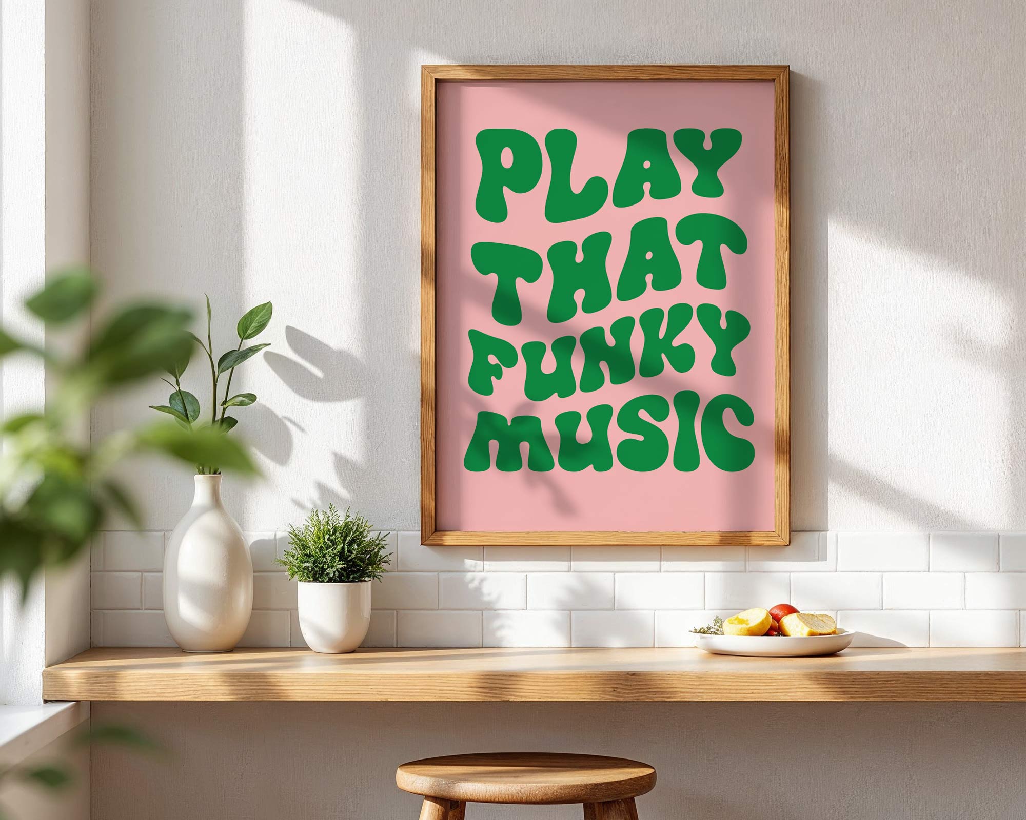 Framed poster with 'Play That Funky Music' text on a pink background in a room with a wooden shelf and plants.