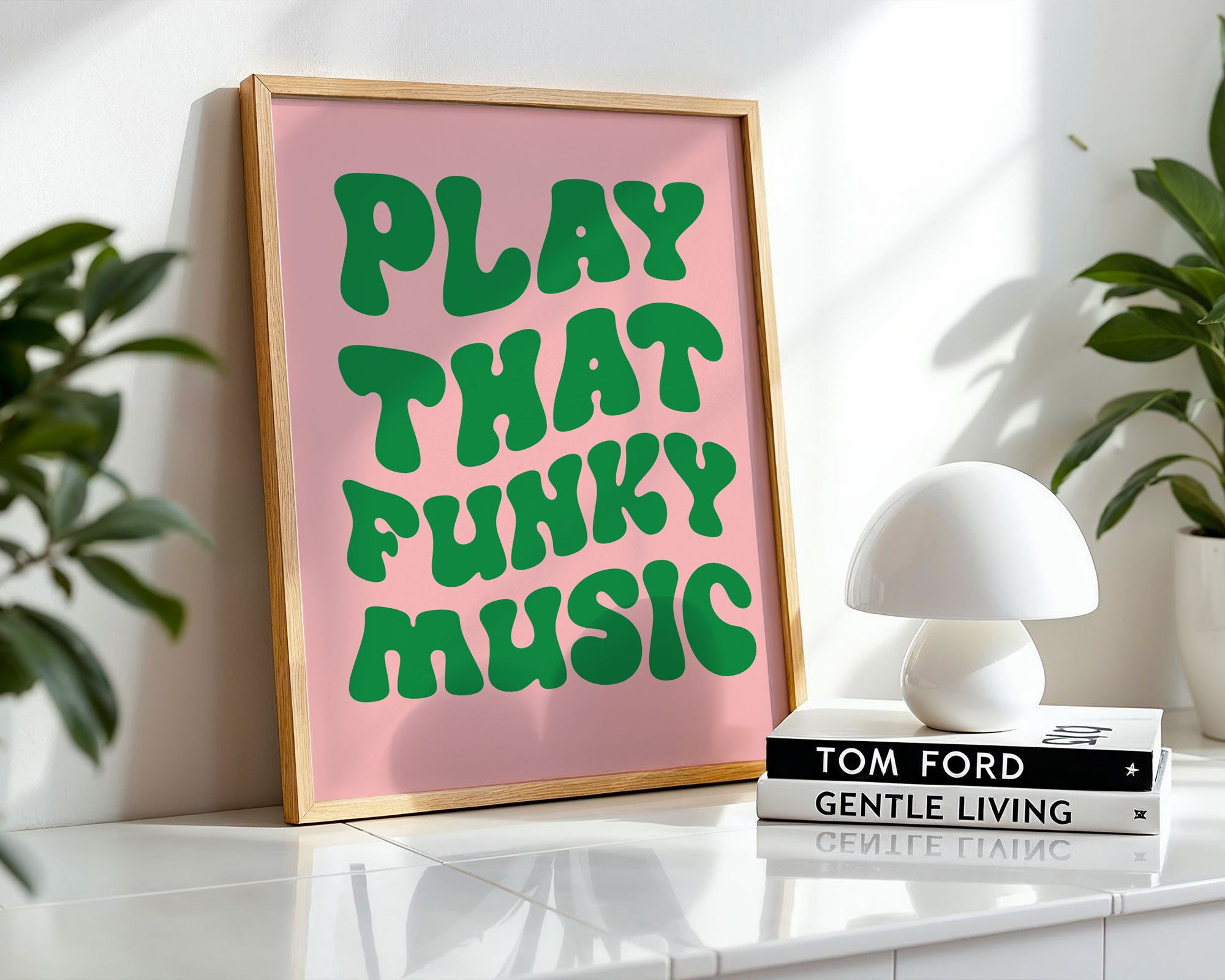 Framed poster with 'Play That Funky Music' text on a pink background, placed on a surface with books and a lamp.