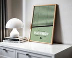 Framed poster of 'Rear Window' on a white surface with a lamp and books.