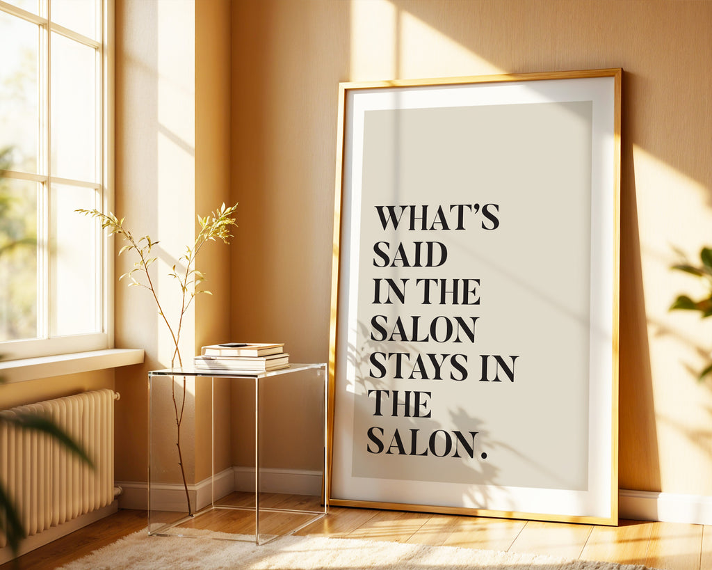 Framed poster with text 'What's said in the salon stays in the salon' in a sunlit room.