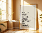 Framed poster with text 'What's said in the salon stays in the salon' in a sunlit room.
