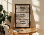 Framed shower karaoke tickets on a wooden table with a plant in the background
