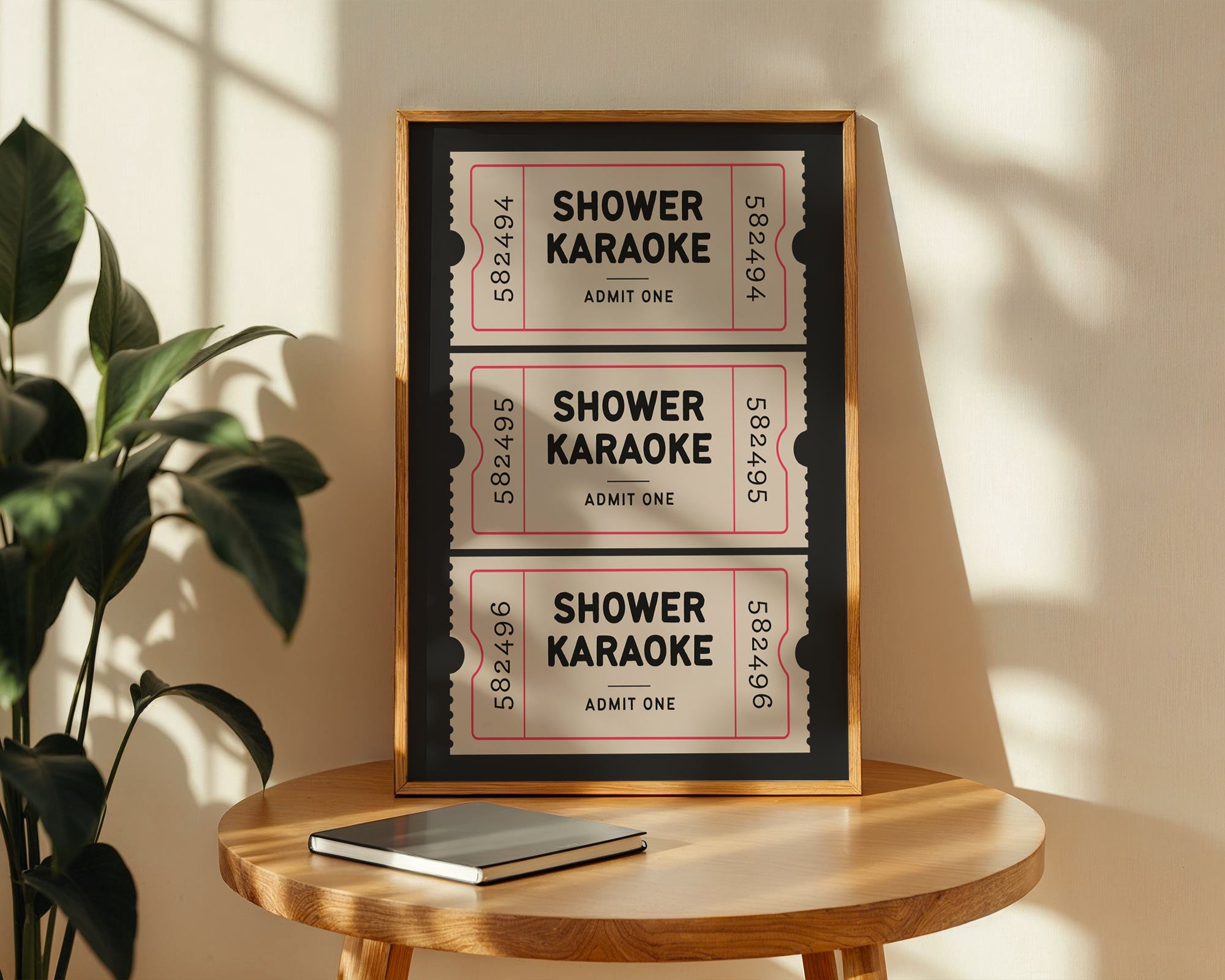 Framed shower karaoke tickets on a wooden table with a plant in the background