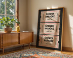Framed 'Shower Karaoke' poster on a wall next to a wooden sideboard with a plant.