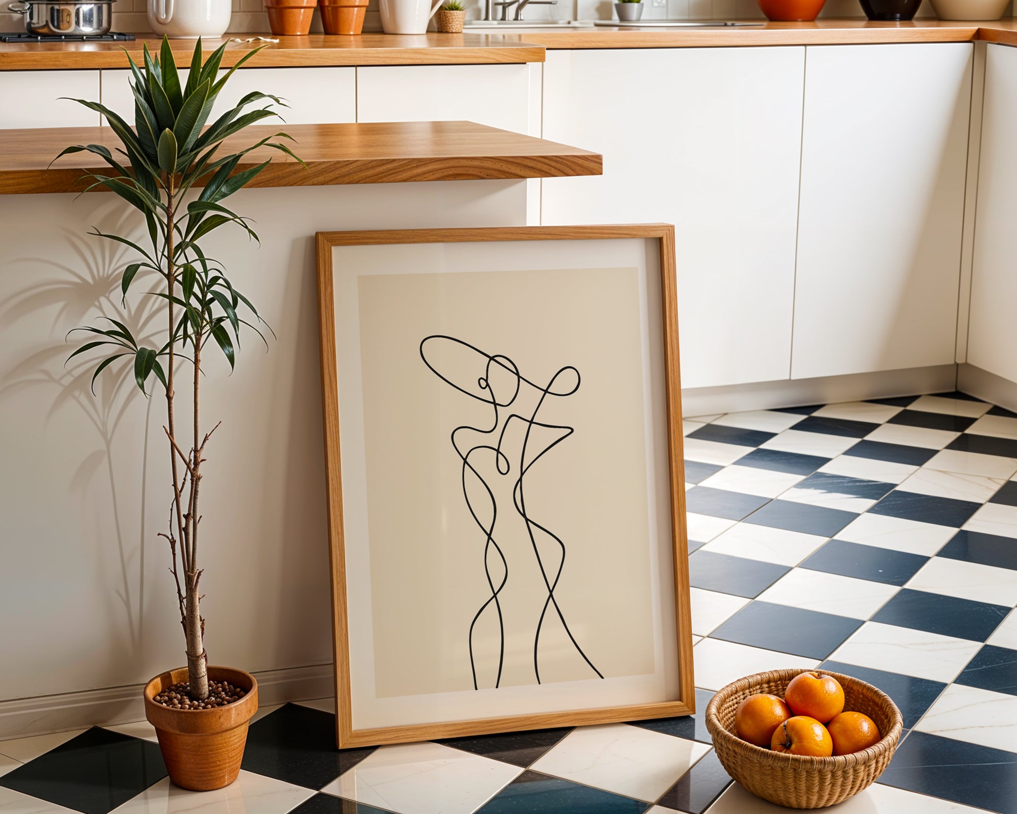 Framed abstract artwork on a checkered floor with a plant and basket of oranges.